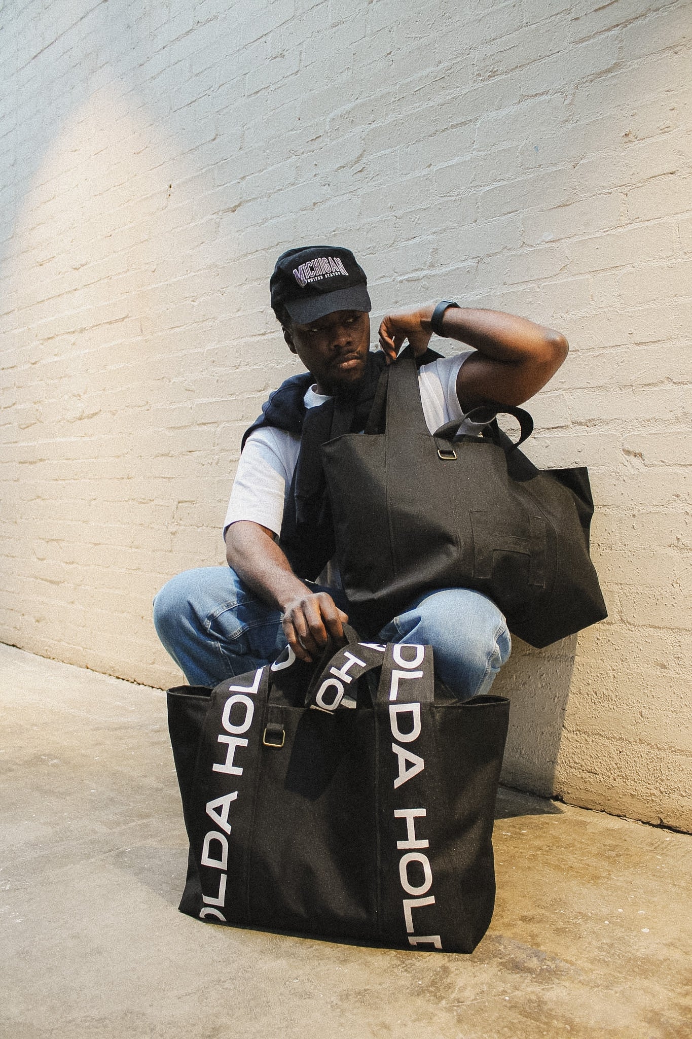 Person holding a black bag with 'HOLDA' branding against a light brick wall.