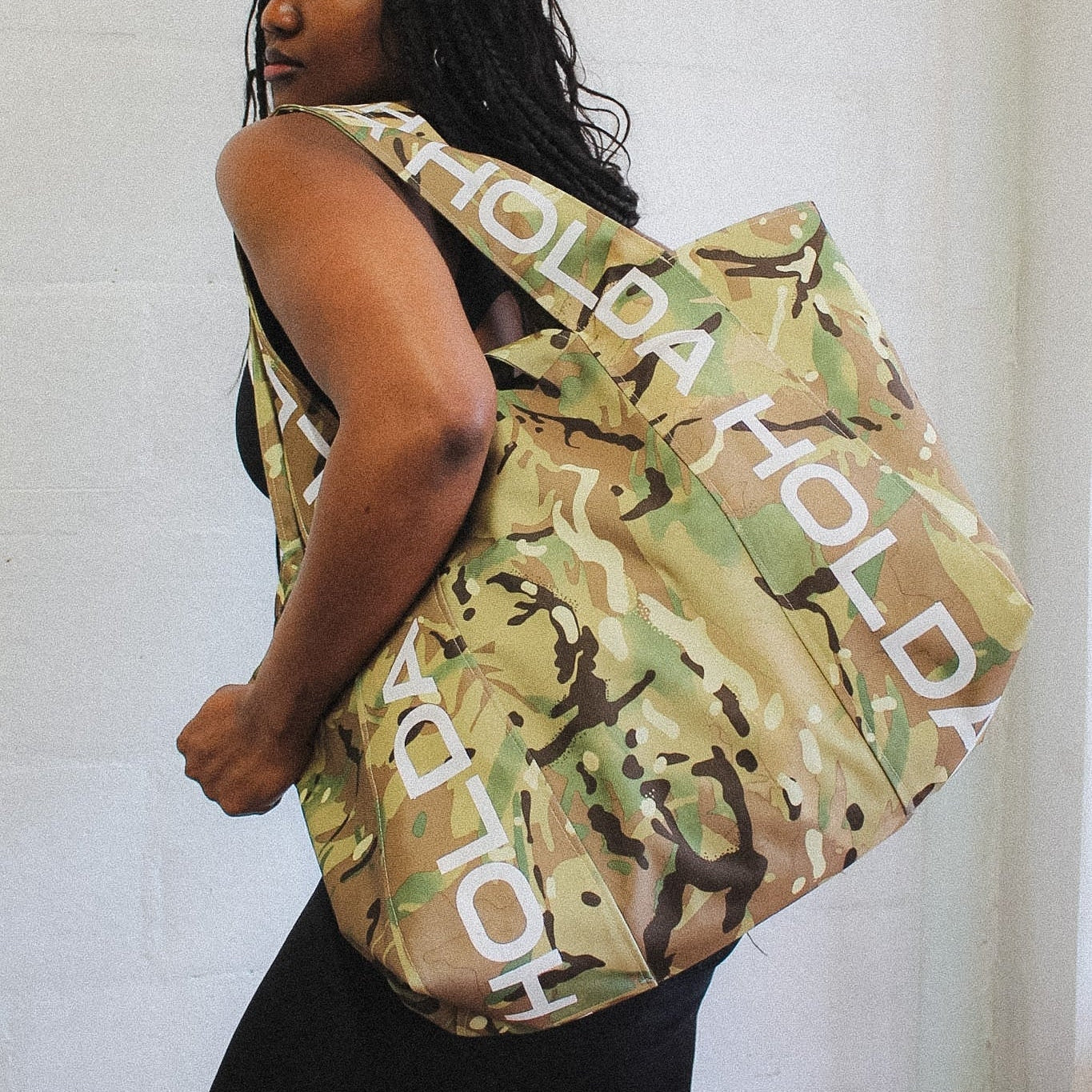 Person holding a camouflage-patterned bag with 'HOLDA' branding.