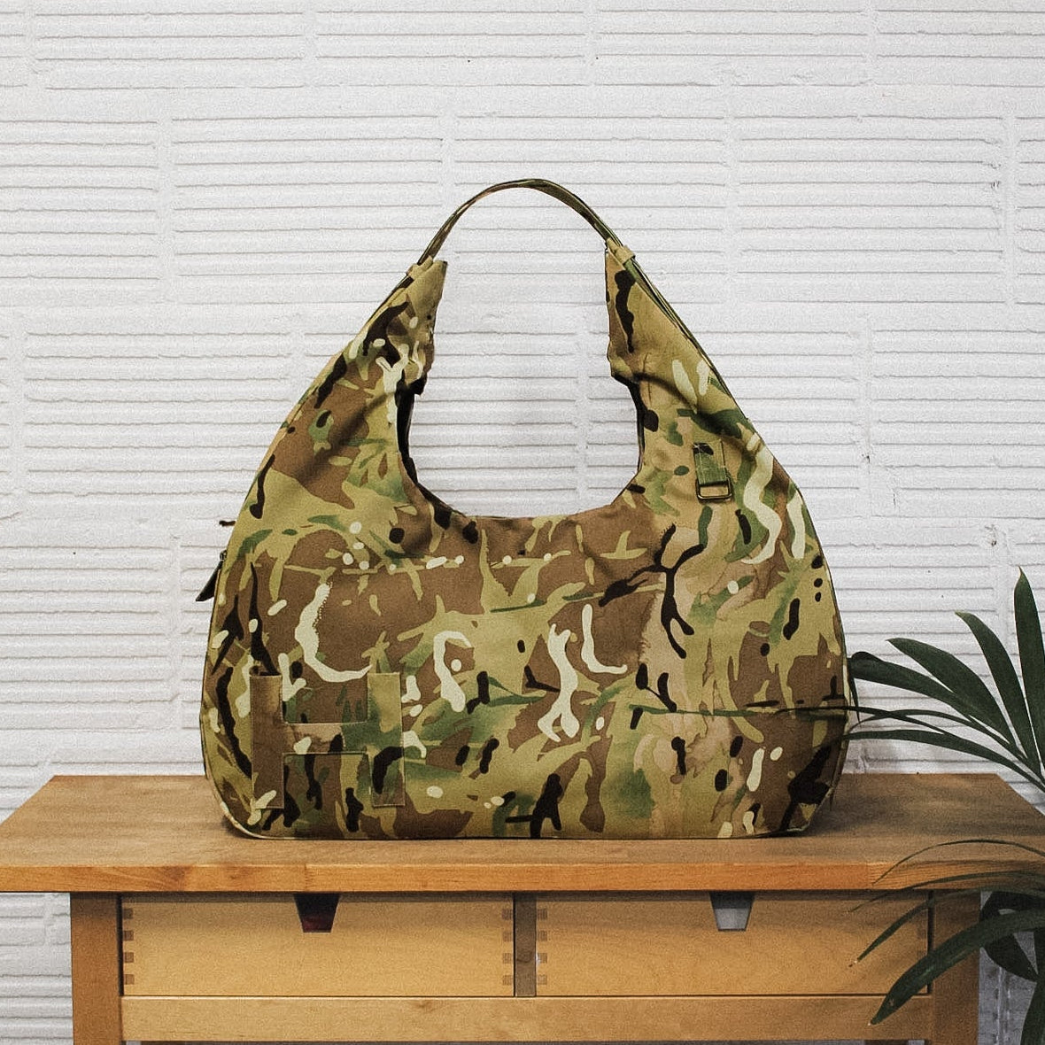 Camouflage handbag on a wooden table with a white wall background